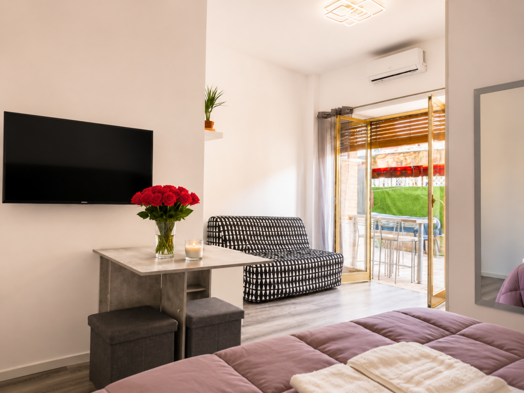 Soggiorno di Aurelia Garden Stay con divano letto, TV, tavolo console allungabile per 6 persone e vista giardino.